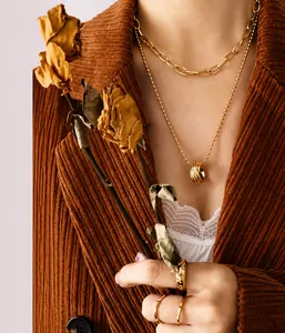 Detail of layered gold stainless steel necklaces with orb pendant and textured link chains
