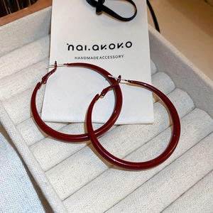 Macro detail of large deep red enamel hoop earrings on beige velvet jewelry display case