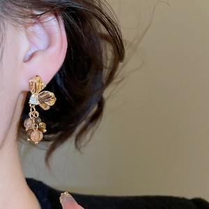 Close-up of golden flower stud earrings with champagne beads on a model's ear