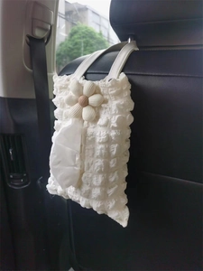 Close-up of cream white floral car tissue box hanging on black leather seat back