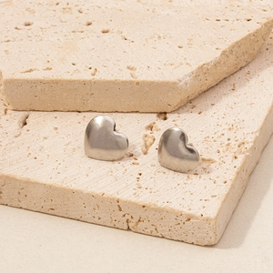 Macro detail of silver heart stud earrings on beige stone showing metallic luster