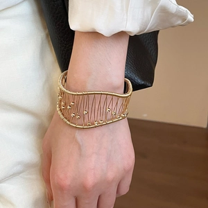 Detail of a wide gold woven mesh cuff bracelet with delicate beads on a wrist