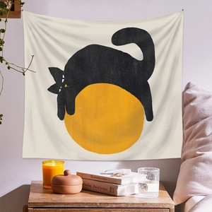 Minimalist black cat wall tapestry hanging above wooden desk with decorative accents
