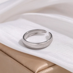 Detailed shot of minimalist silver open ring on white silk with premium gold jewelry box
