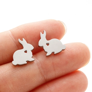 Macro shot of silver rabbit stud earring with heart cutout held on a fingertip