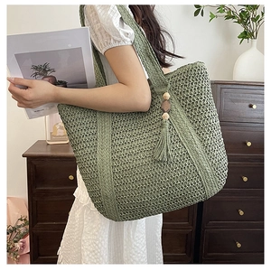 Olive green woven tote bag with fringe wood bead charm shown in a cozy home interior