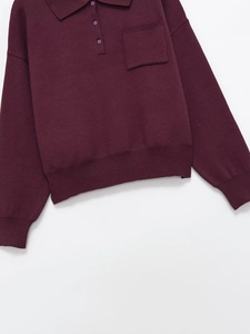 Detail of burgundy knitted polo sweater featuring ribbed cuffs and classic chest pocket