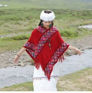 Detail of red knit poncho featuring colorful geometric patterns and decorative fringe hem