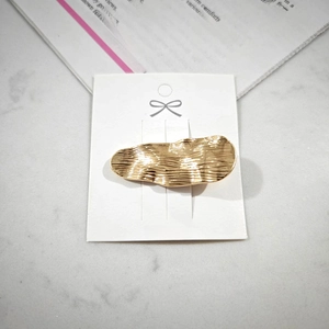 Detail of a golden alloy hair clip with wavy brushed texture on a marble background