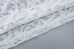 Détail du tissu en dentelle blanche avec motifs floraux et bords ondulés sur la robe