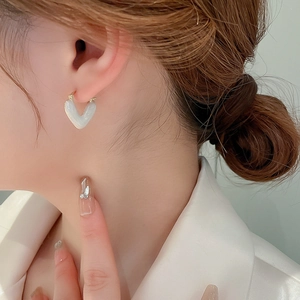 Close-up of model wearing heart-shaped pearl white enamel earrings with gold accents