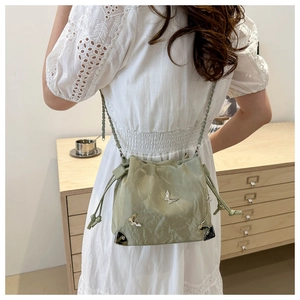 Close-up of mint green bucket bag with metallic butterfly detail and chain strap