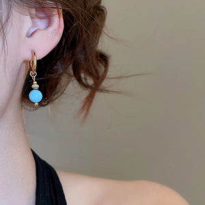 Detailed close-up of vintage gold hoop earrings with turquoise and zircon pendant on model