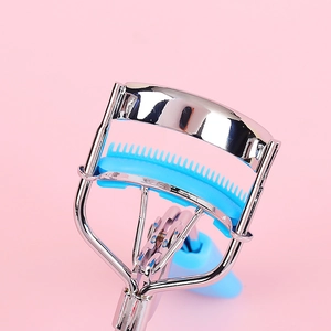 Portable stainless steel eyelash curler with blue comb and silicone pad on pink background