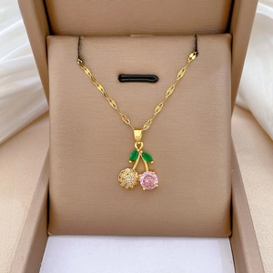 Macro shot of cherry pendant necklace with pink gems and gold chain on silk