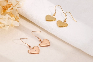 Detail of gold and rose gold heart earrings with zircon inlay on beige fabric background
