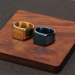 Polished stainless steel square signet rings in gold and deep blue on wood base