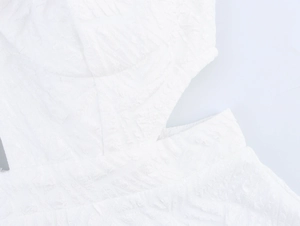 Macro detail of white dress featuring intricate embossed floral texture and hollow cut-outs