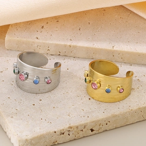 Close-up of gold and silver steel rings with colorful zircons on a textured stone