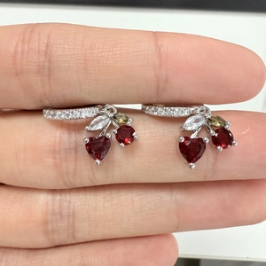 Macro shot of silver cherry earrings with red heart gems and sparkling leaf accents