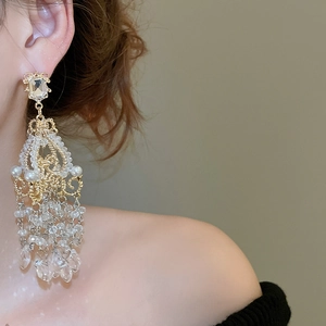 Close-up of elegant gold tassel earrings with pearls and crystals worn on model