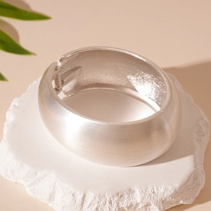 Detail of silver matte brushed wide metal cuff bracelet on white stone base