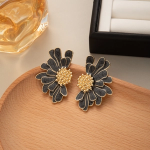 Detail of floral earrings with black petals and gold stamen on a wooden tray