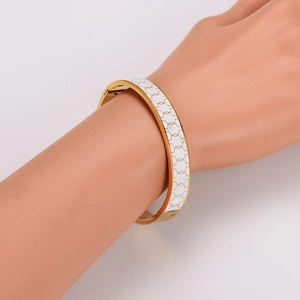 Polished gold 304 stainless steel bangle with white enamel inlay on a model's wrist