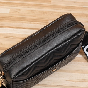 Close-up of black chevron quilted crossbody bag with gold zipper and woven strap