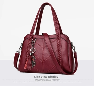 Detail of burgundy textured leather handbag featuring V-shaped stitching and tassel charm