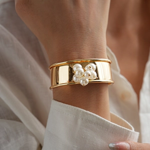 Detailed view of wide gold metal cuff bracelet with white pearl flower decoration