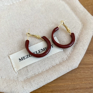 Detail of burgundy C-shaped resin hoop earrings with gold metal studs on a fabric pouch