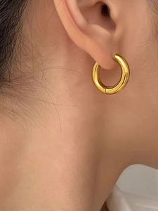 Macro side view of a polished chunky gold hoop earring worn by a model