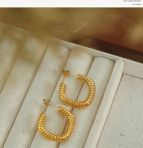 Macro shot of gold twist texture C-shape earrings displayed in a luxury white jewelry box