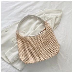 Detailed texture of beige woven straw shoulder bag with a wide white strap and hollow design