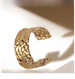 Macro detail of wide hammered gold cuff bracelet with irregular textured light reflections