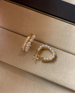 Close-up of golden C-shaped earrings with white pearls and sparkling zirconia details