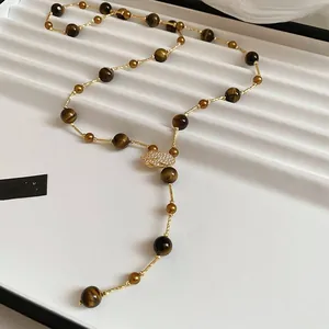 Detailed close-up of tiger eye bead necklace with gold twist chain and zircon leaf charm