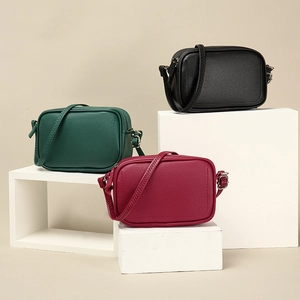Three minimalist crossbody camera bags in black, dark green, and wine red with lychee texture