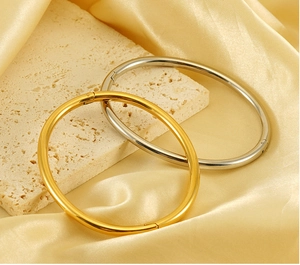 Polished gold and silver oval titanium steel bracelets on a beige travertine stone