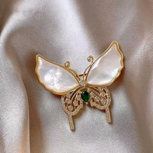 Macro detail of butterfly brooch with shell inlay, green gem, and gold plating
