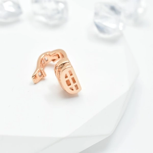 Rose gold connector clasp with lattice texture and inlaid gems on white platform