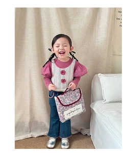 Detail of child wearing a floral print handbag with stylish knit vest and denim outfit