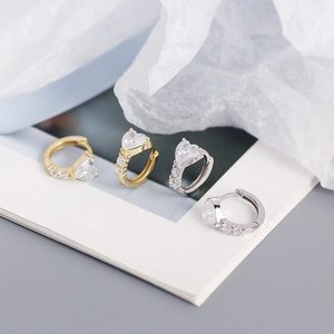 Macro detail of gold and silver heart-shaped zircon earrings with micro-inlaid side crystals