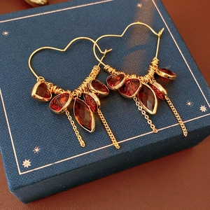 Detail of 18K gold-plated heart hoop earrings with red crystal pendants and fringe tassels