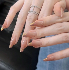 Macro detail of nude almond press-on nails with golden French tips and metallic finish