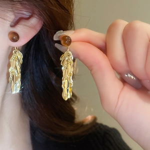 Detail of golden tassel earrings featuring brown resin beads worn on a female model