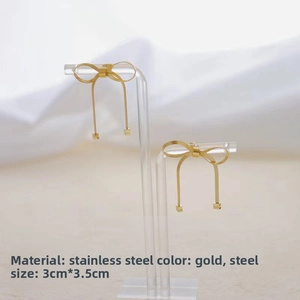 Detail of golden stainless steel bow earrings with square charms on acrylic stand