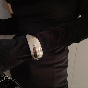 Detail of wide open silver bangle with polished mirror finish worn over black velvet sleeve