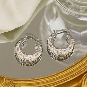 Detail of silver vintage hoop earrings with embossed floral patterns on mirror